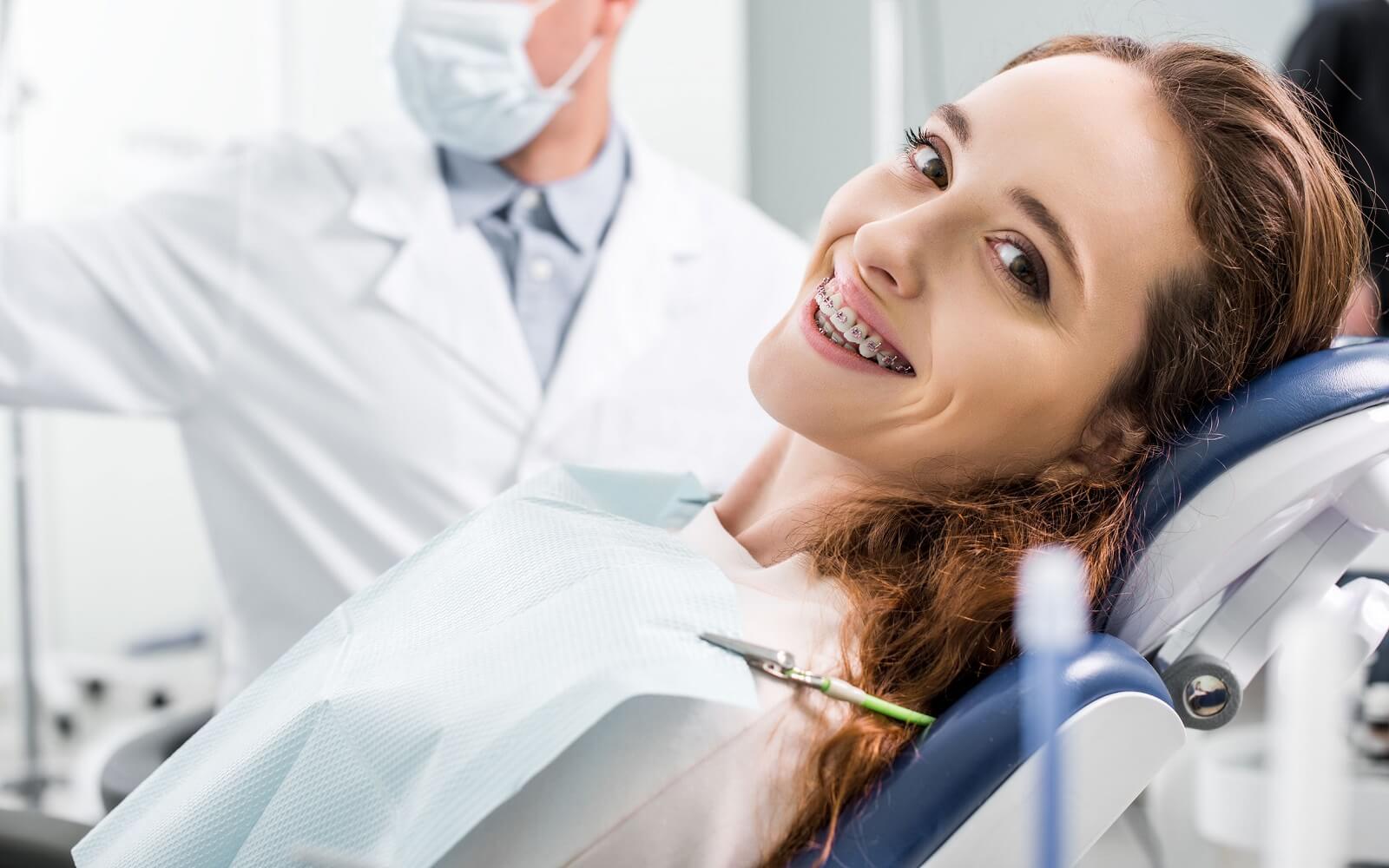 Junge Frau mit Zahnspange lächelt entspannt auf einem Stuhl in moderner Zahnarztpraxis.