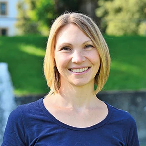 Porträt einer lächelnden Frau im Park vor grüner Wiese und unscharfem Hintergrund.