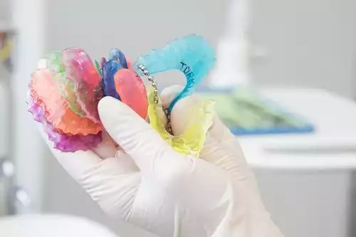 Eine Hand mit Handschuh hält bunte Zahnspangen in einer Zahnarztpraxis.